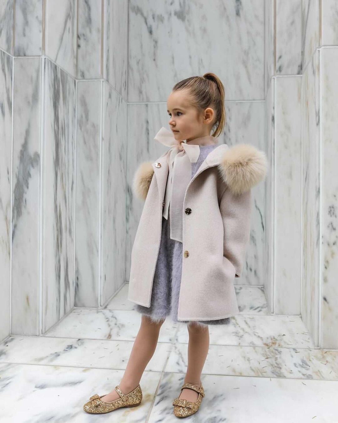 A kid wearing a beige cashmere and fur coat designed by MVFURS.