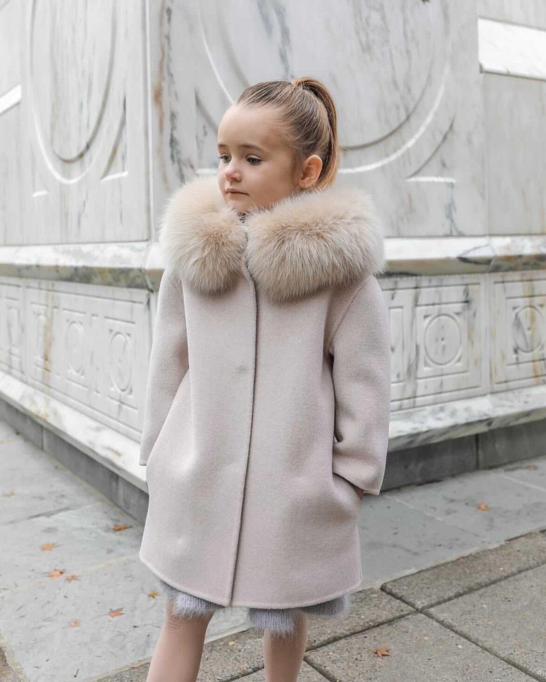 A kid wearing a beige cashmere and fur coat designed by MVFURS.