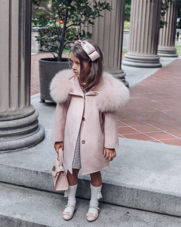 A kid wearing a light pink cashmere and fur coat called designed by MVFURS.