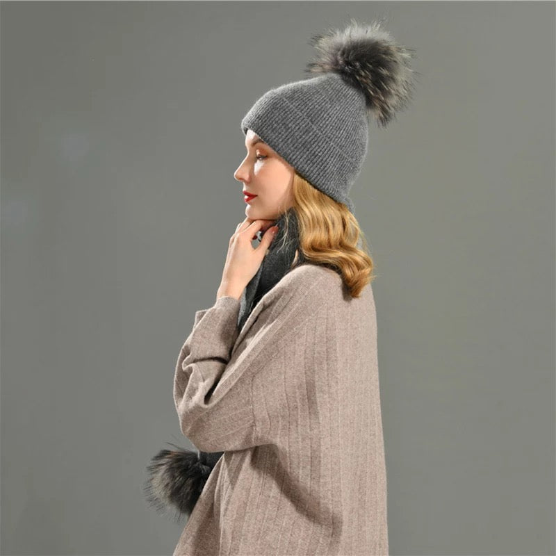 A woman wearing a grey cashmere scarf and pom pom fur hat designed by MVFURS
