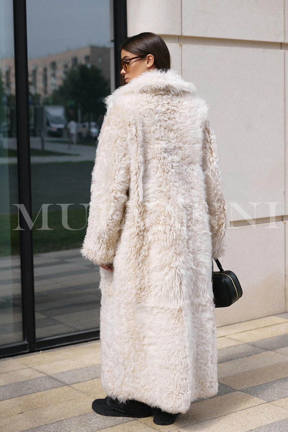 Ankle-length beige shearling coat for women, with a fluffy, insulating lining and a sleek, minimalist design. It includes a wide collar and understated button details, perfect for staying warm in colder weather while looking chic.