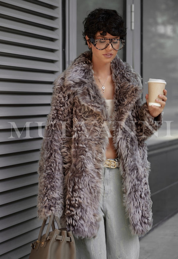 Woman wearing ADRIE Mousse Shearling Coat, holding coffee, and carrying a handbag, showcasing luxurious and cozy fashion.