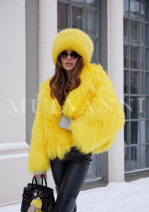 A woman wearing a vibrant yellow Mongolian fur coat paired with a matching yellow fur hat. She carries a stylish black bag, creating a bold and fashionable look perfect for winter outings.