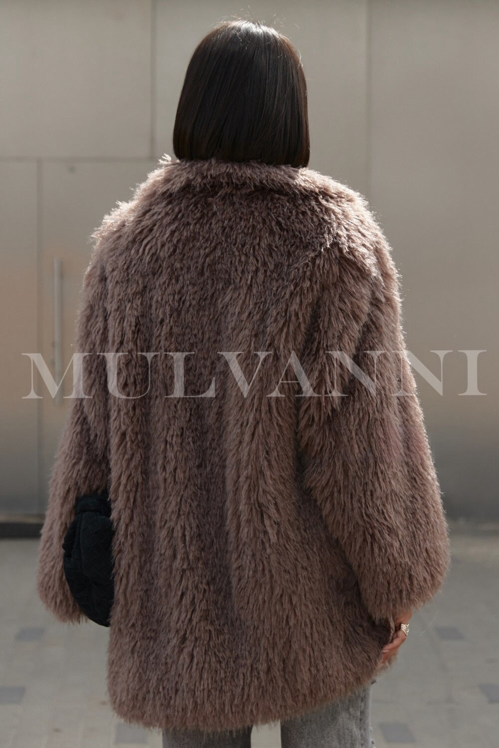 A woman wearing a chic brown faux Mongolian coat paired with modern sunglasses. The coat’s rich texture and sophisticated silhouette offer both warmth and elegance, perfect for winter outings.