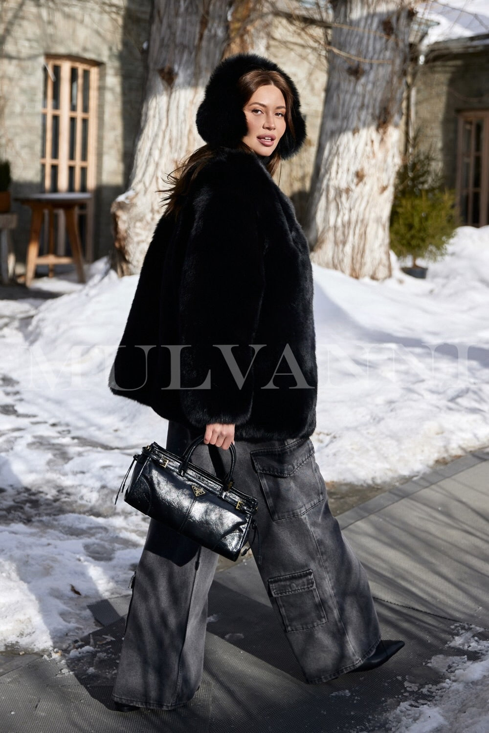 A woman adorned in a plush black fox fur coat, exuding elegance with its luxurious texture, paired with snug black ear warmers. The combination offers a stylish and warm solution for winter outings.