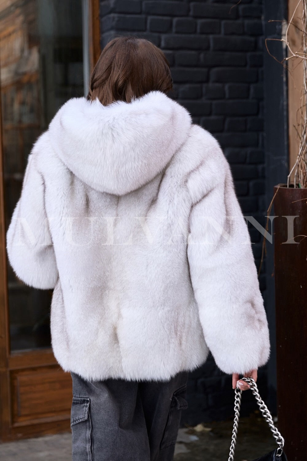 A woman wearing a high-quality hooded plush white fox fur coat, designed to offer exceptional warmth and elegance. The coat's soft, fluffy exterior and cozy hood create a chic look ideal for winter outings.