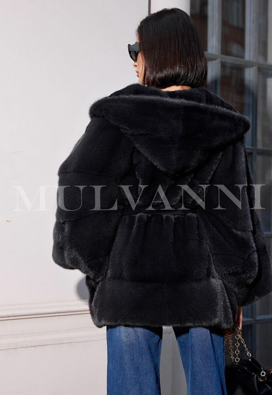 Woman wearing an ALEXANDRA Hooded Mink black Coat, showcasing its luxurious and stylish design from the back.