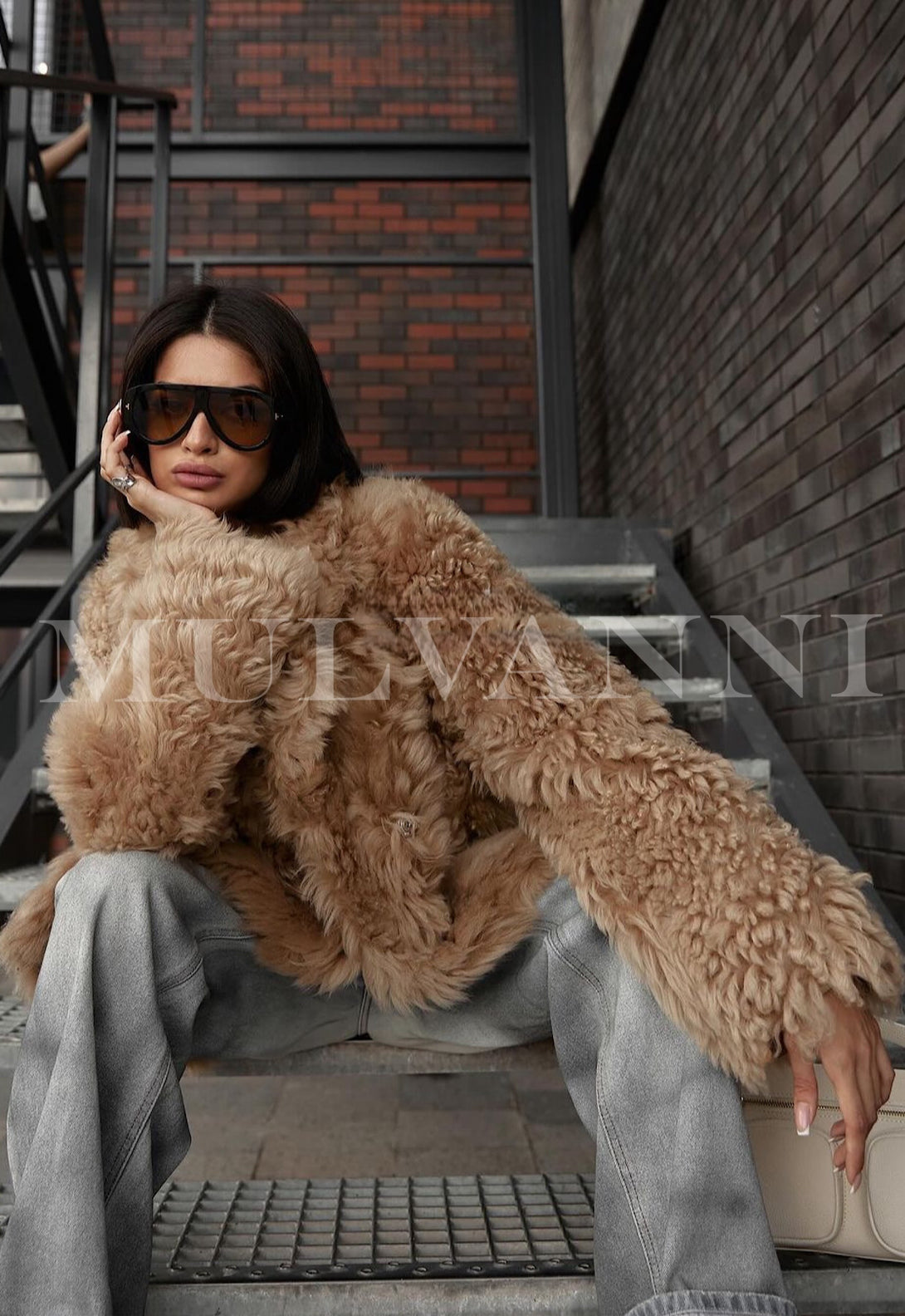 Woman wearing stylish ecru shearling coat, sitting on stairs, exuding elegance and confidence in urban setting