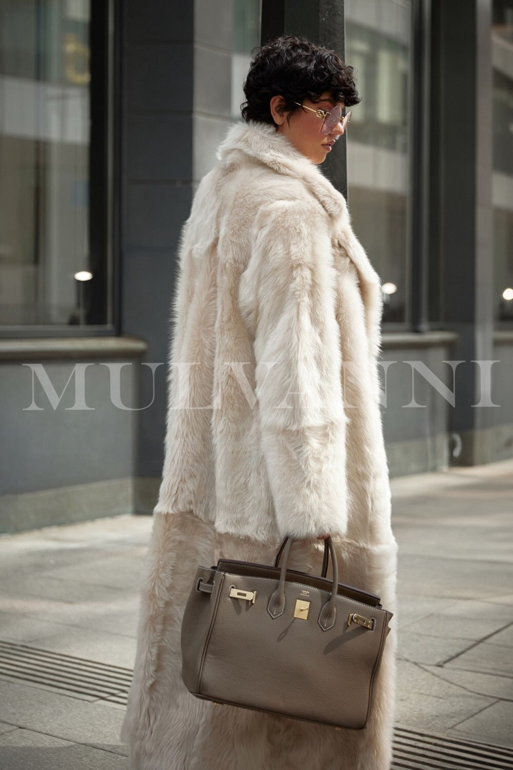 A woman wearing an exquisite long beige shearling coat, known for its exceptional quality and cozy warmth. The coat features an elegant silhouette that adds a touch of sophistication to her winter wardrobe.