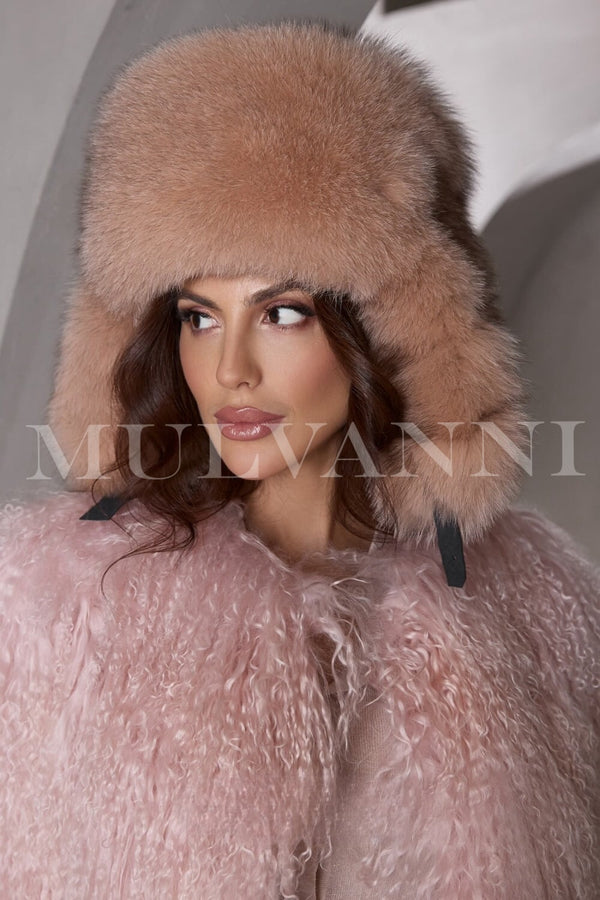 A woman wearing a camel fox fur hat, featuring a soft, luxurious texture and a snug fit. The hat has a stylish, rounded design that frames her face, adding an elegant touch to her winter outfit.