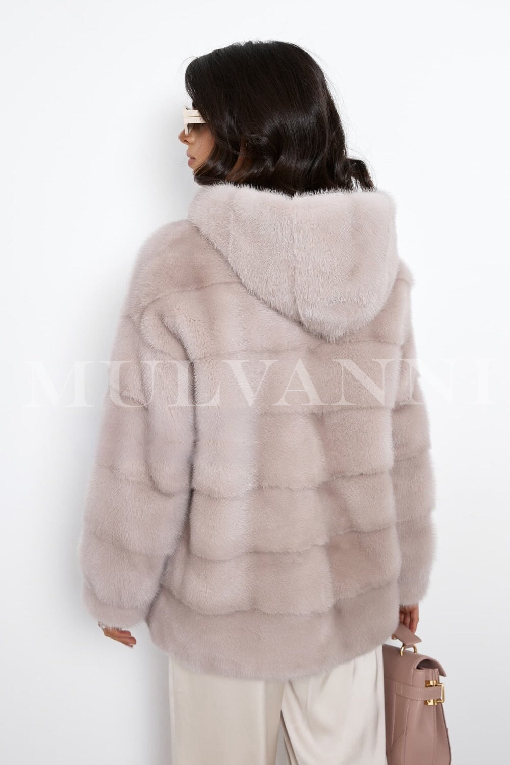 A stylish short beige mink fur coat worn by a woman, featuring a cozy hood and sleek zipper closure. The coat has a refined, soft texture and a fitted design, making it a fashionable and practical choice for winter.