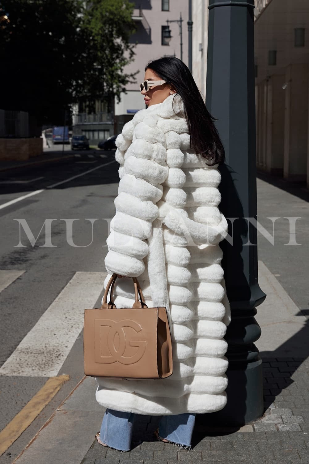 A woman dressed in an elegant long white faux fur coat, featuring a soft, high-end texture and a matching belt that enhances her silhouette. The coat’s flowing design and sophisticated look make it perfect for stylish winter outings.