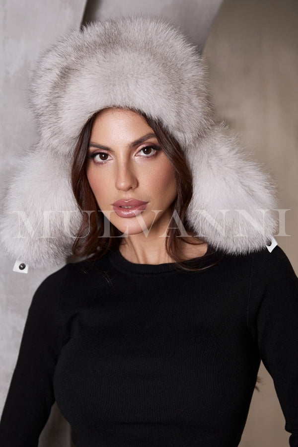 A woman wearing a grey fox fur hat, featuring a soft, luxurious texture and a snug fit. The hat has a stylish, rounded design that frames her face, adding an elegant touch to her winter outfit.