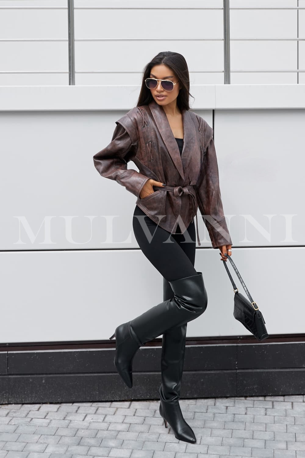 A woman wearing a trendy brown leather jacket, cinched at the waist with a matching belt. The modern design and elegant details make it a versatile choice for both casual and formal occasions.