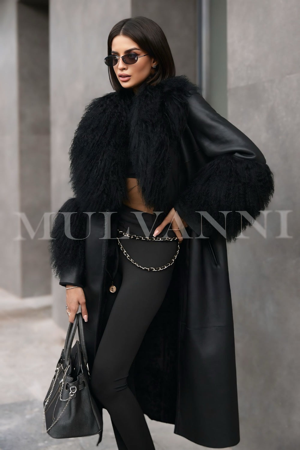 A woman dressed in a black leather trench coat with luxurious Mongolian fur accents at the collar and cuffs. The coat's tailored fit and elegant details create a sophisticated look, perfect for colder weather.