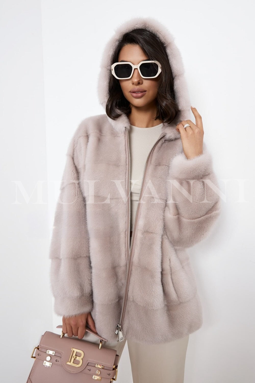 A woman wearing a beige mink fur coat with a hood and zipper closure. The coat is cropped for a trendy silhouette, offering a cozy, elegant feel with its plush fur texture, perfect for cold-weather outings.