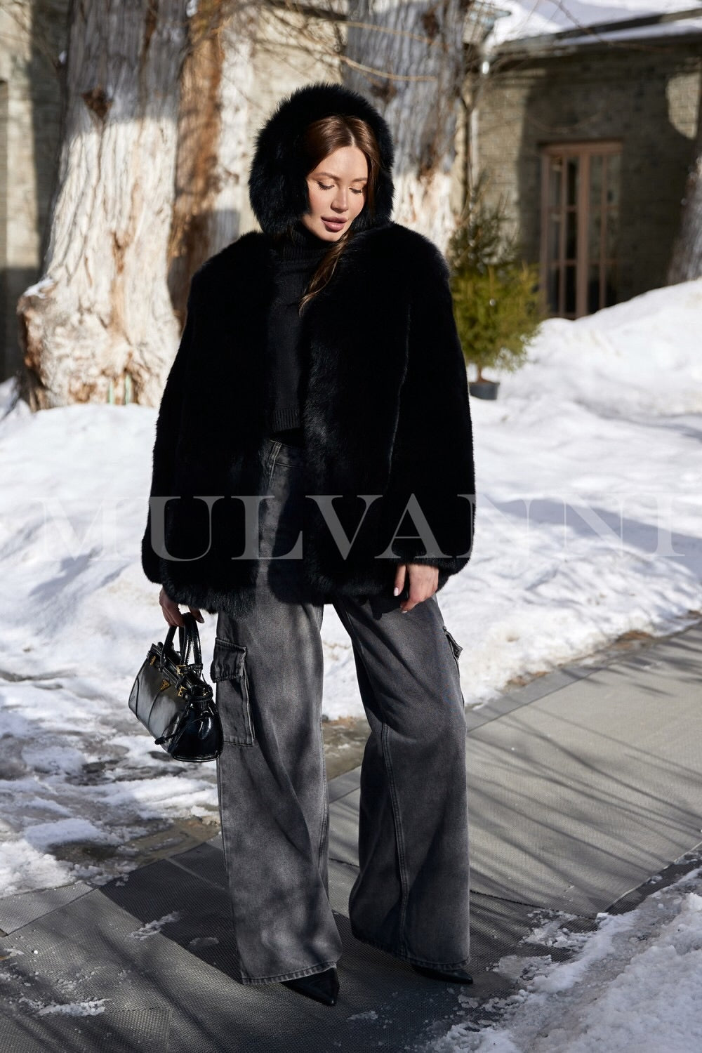 A woman in a luxurious black fox fur coat, featuring a soft and voluminous design, complemented by black ear warmers. The ensemble provides both warmth and sophistication for cold-weather fashion.