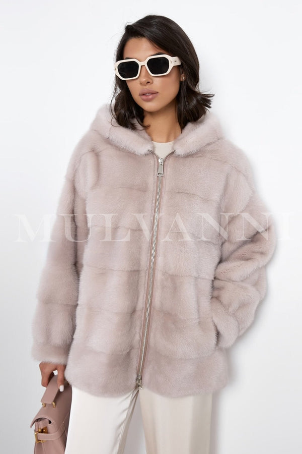 A woman wearing a short beige mink fur coat with a soft, plush texture. The coat features a hood and a sleek front zipper closure, providing a cozy, stylish look perfect for staying warm in the winter."