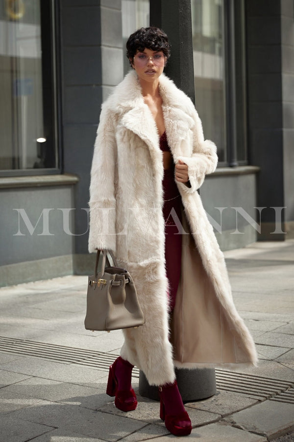 A woman wearing a long beige shearling coat that exemplifies high quality and luxury. The coat features a soft, plush texture and an elegant silhouette, providing warmth and sophistication for winter occasions.