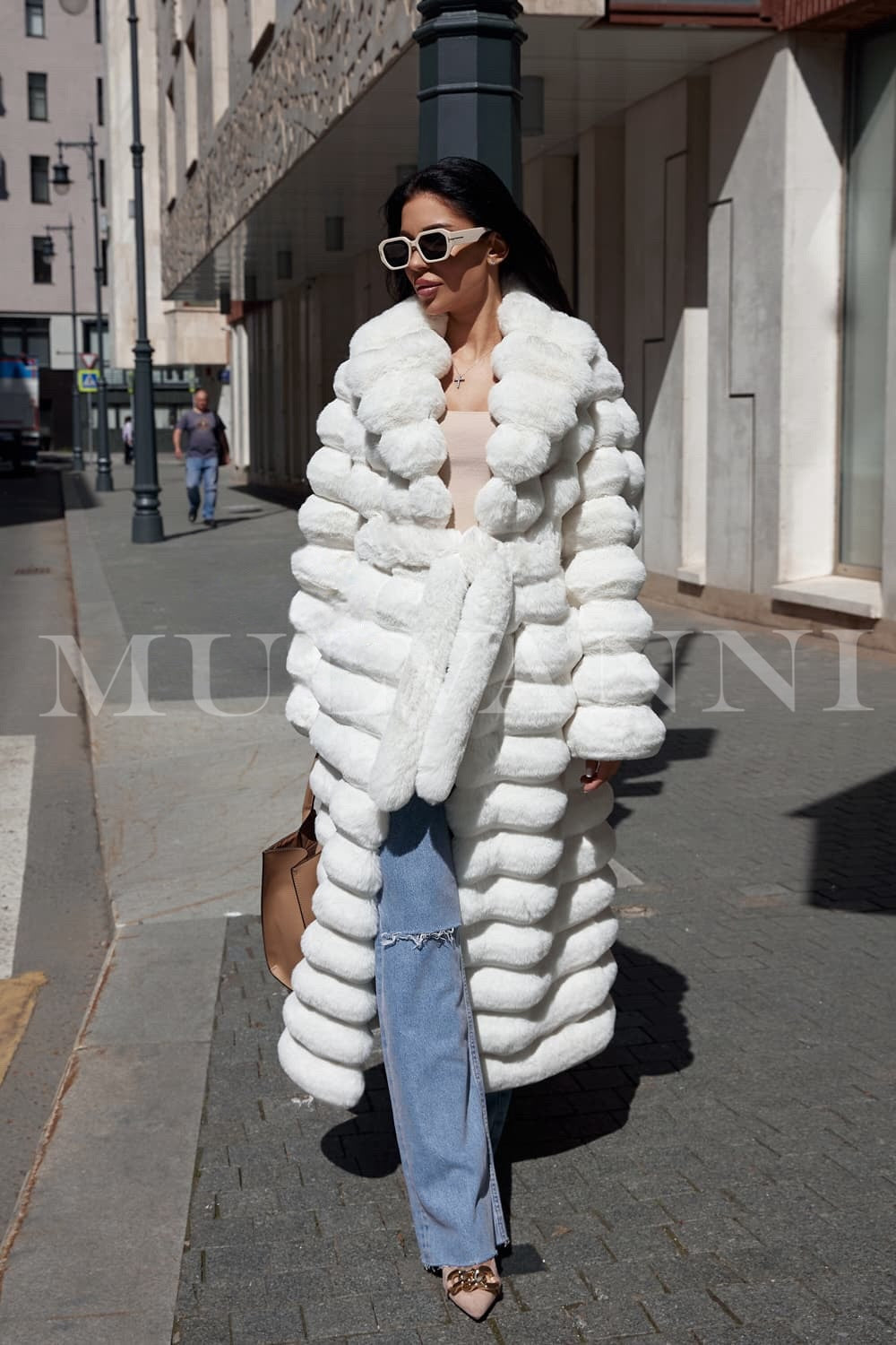 A woman in a long white faux fur coat, showcasing a plush, premium texture and a matching belt for a tailored look. The coat flows elegantly to the ground, adding a touch of glamour and warmth for winter occasions.