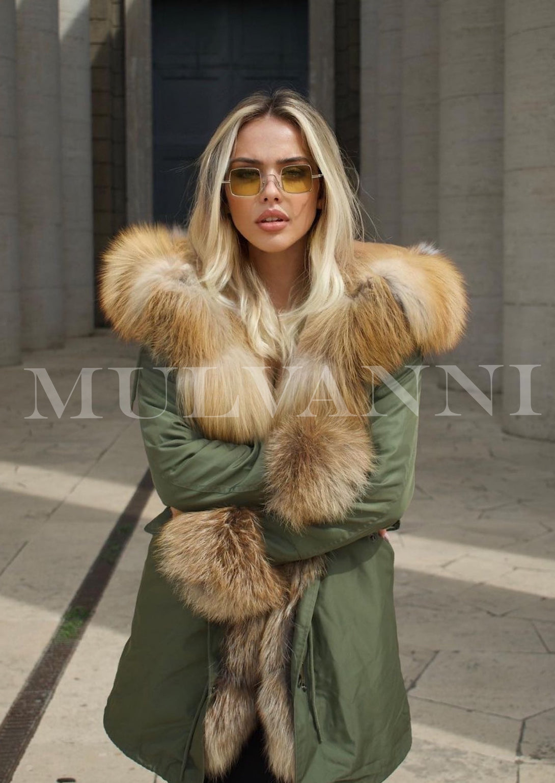 A woman wearing a green parka lined with luxurious red fox fur. The vibrant fur detail adds warmth and style, creating a chic winter look perfect for cold weather.