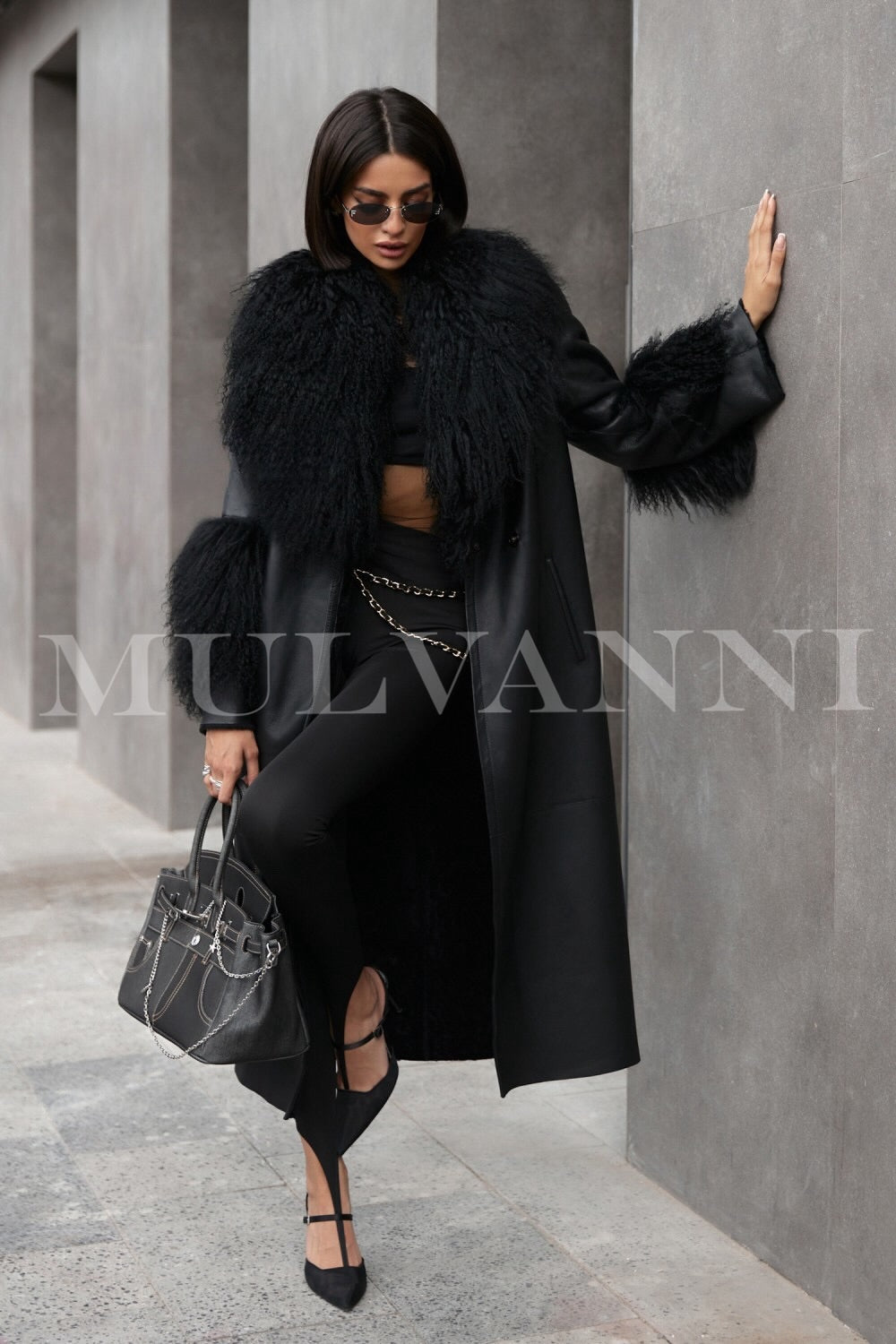 A woman in a stylish black leather trench coat, featuring a plush Mongolian fur collar and cuffs. The coat blends edgy leather with soft fur, making it a fashionable choice for winter outings.