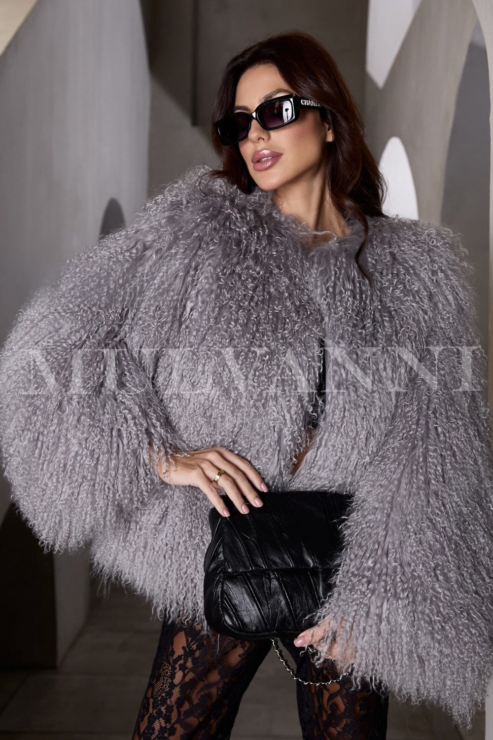 A woman wearing a stylish grey Mongolian fur coat, featuring a soft, textured exterior and a cozy fit. The coat has a short-length design with wide lapels and an open front, exuding elegance and warmth.