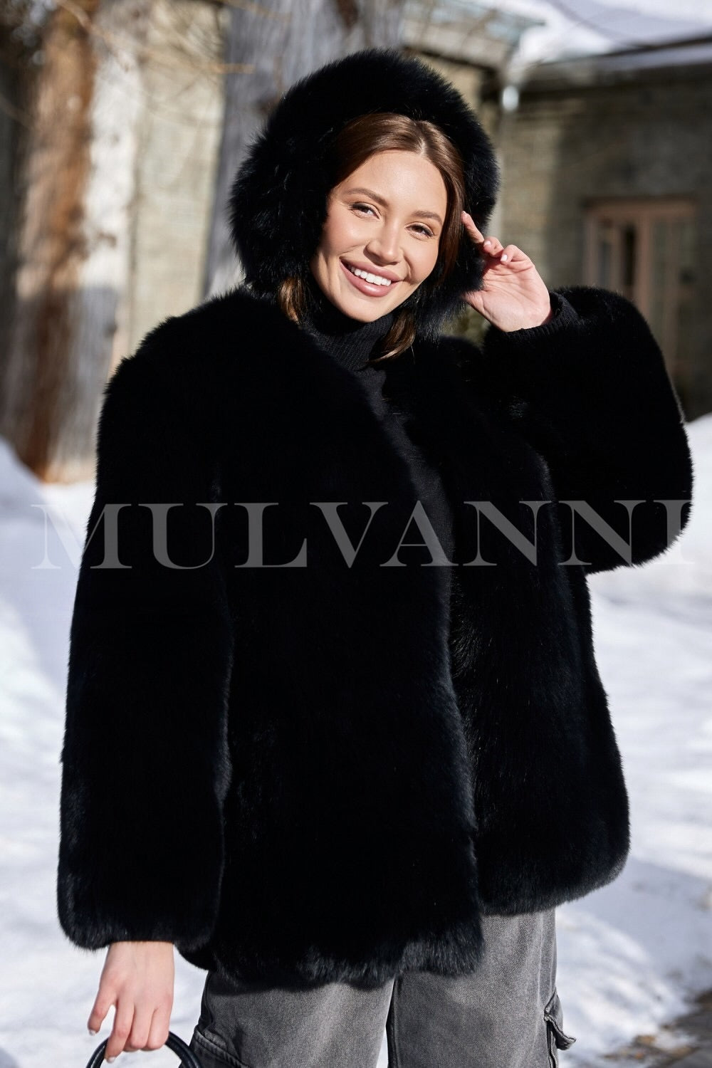 A woman wearing a stylish plush black fox fur coat, showcasing a rich, fluffy texture, paired with black ear warmers. The coat's tailored fit enhances her silhouette, creating a chic and cozy winter outfit.