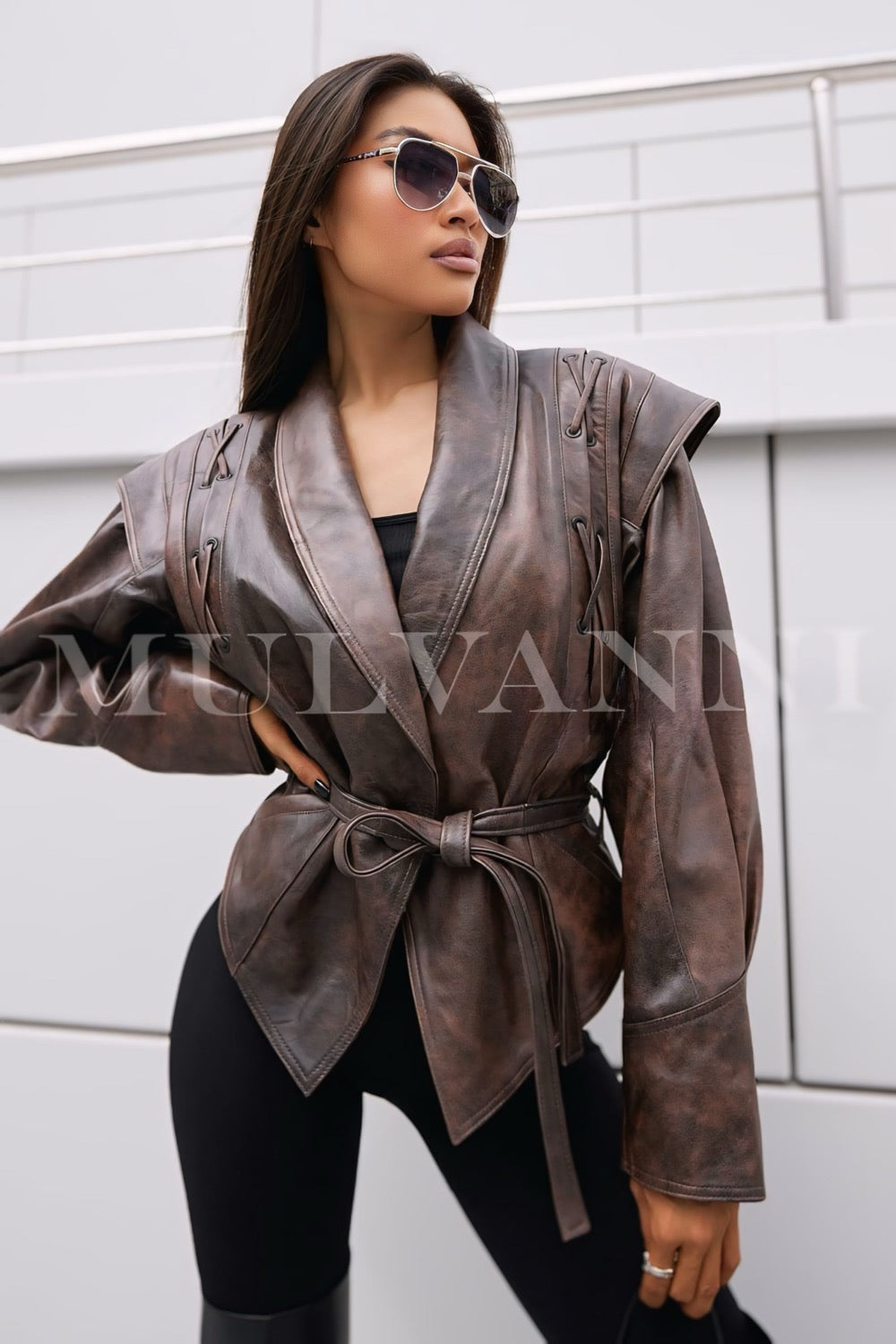 A woman in a stylish brown leather jacket with a contemporary cut, complemented by a matching belt. The jacket's fitted silhouette and high-quality leather add sophistication to her outfit.