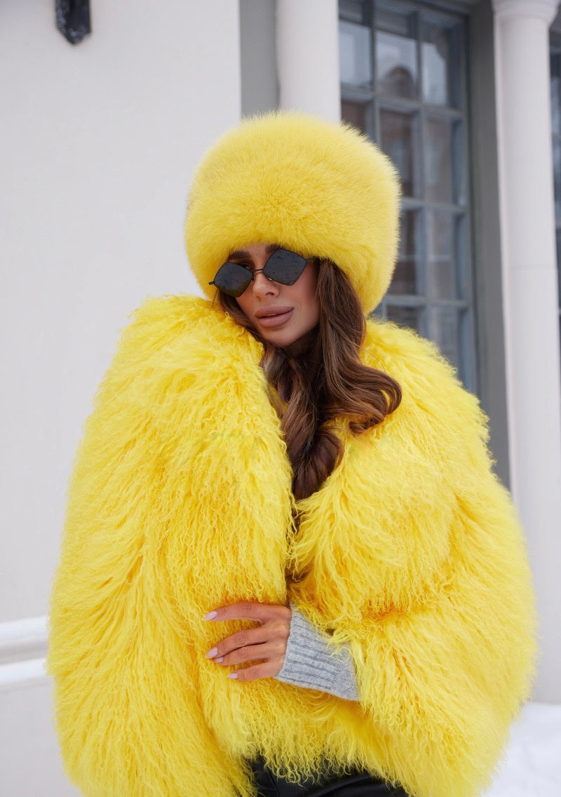 A woman in a striking yellow fox fur hat that complements her matching Mongolian fur coat. The hat has a soft, fluffy texture, and the coat features a luxurious, flowing design, making for a bold and stylish winter ensemble.