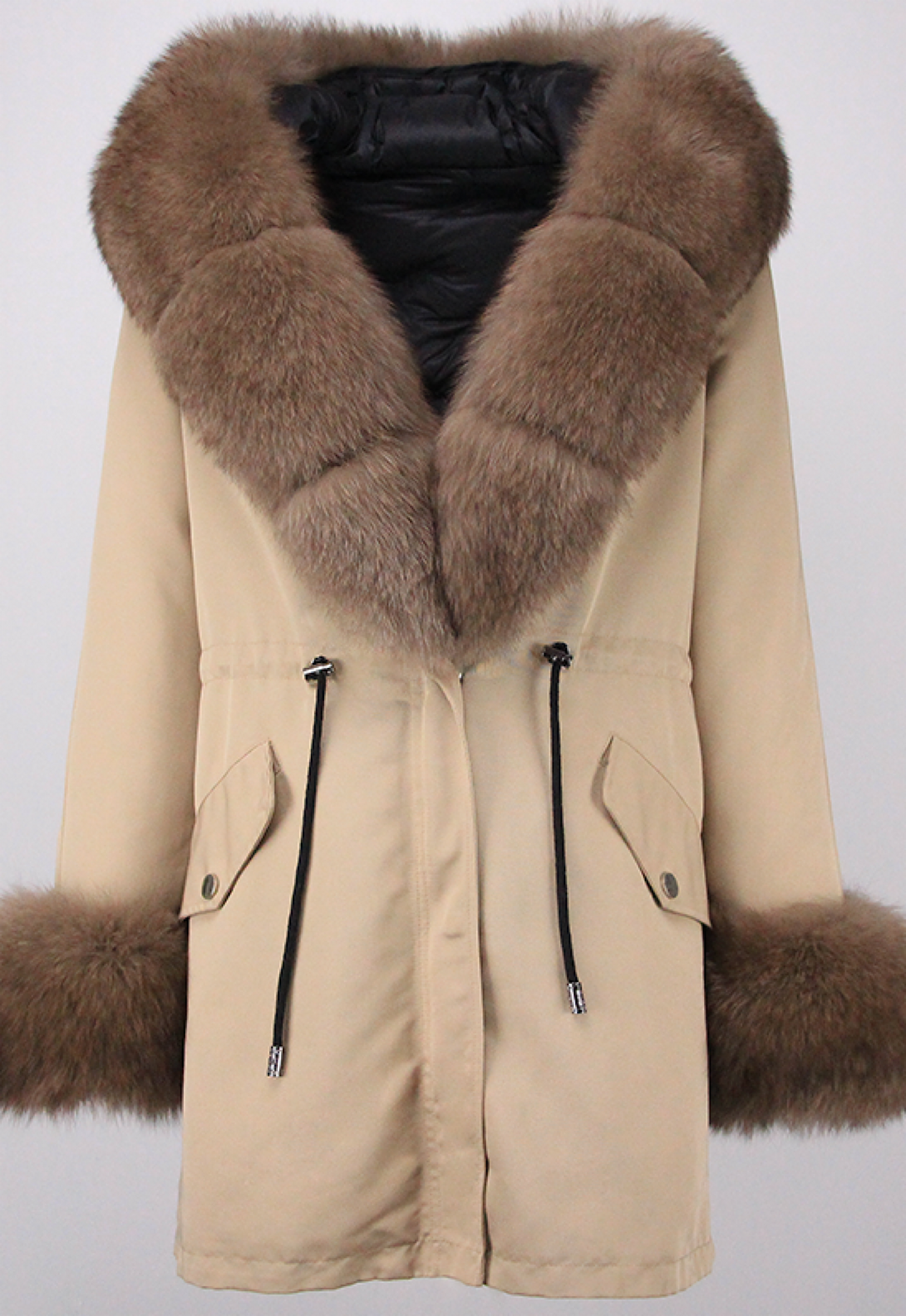 A woman wearing a beige hooded parka accented with plush brown fox fur trim and cuffs. The combination of colors and textures provides a chic and cozy option for cold-weather fashion.