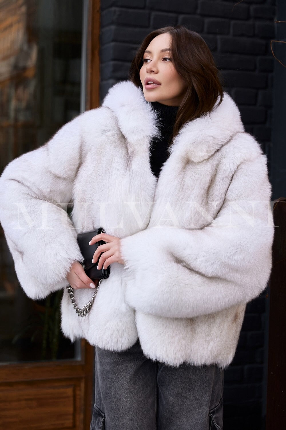 A woman wearing a high-quality hooded plush white fox fur coat, designed for warmth and elegance in cold winter weather. The coat features a soft, luxurious texture and a cozy hood, creating a stylish and protective outer layer.