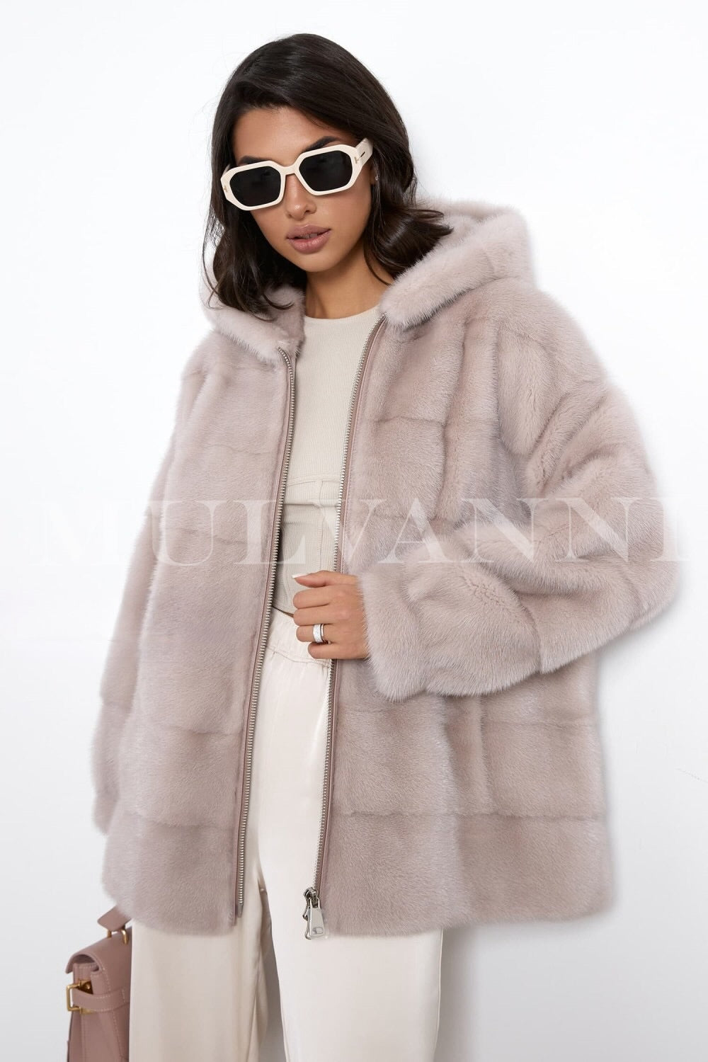 A woman in a short beige mink fur coat, featuring a luxurious hood and a front zipper closure. The coat has a soft, velvety finish and a fitted design, combining warmth with a chic, modern look for winter.