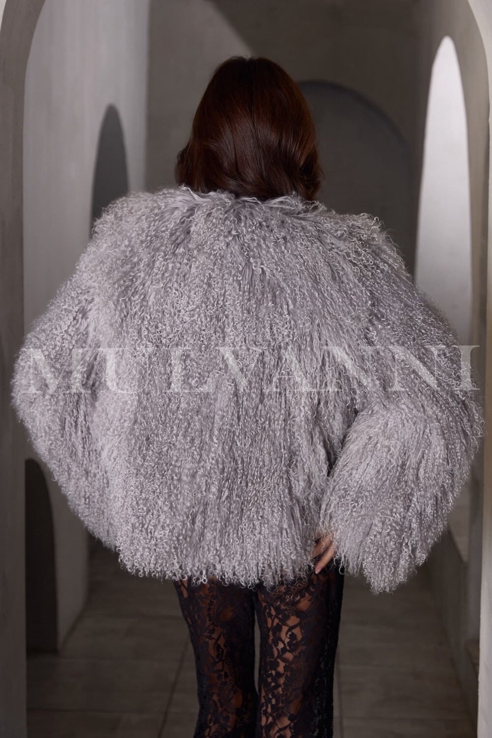 A woman adorned in a fashionable grey Mongolian fur coat, highlighting its rich texture and mid-length style. The coat features an unstructured fit and wide lapels, creating a warm and elegant appearance.