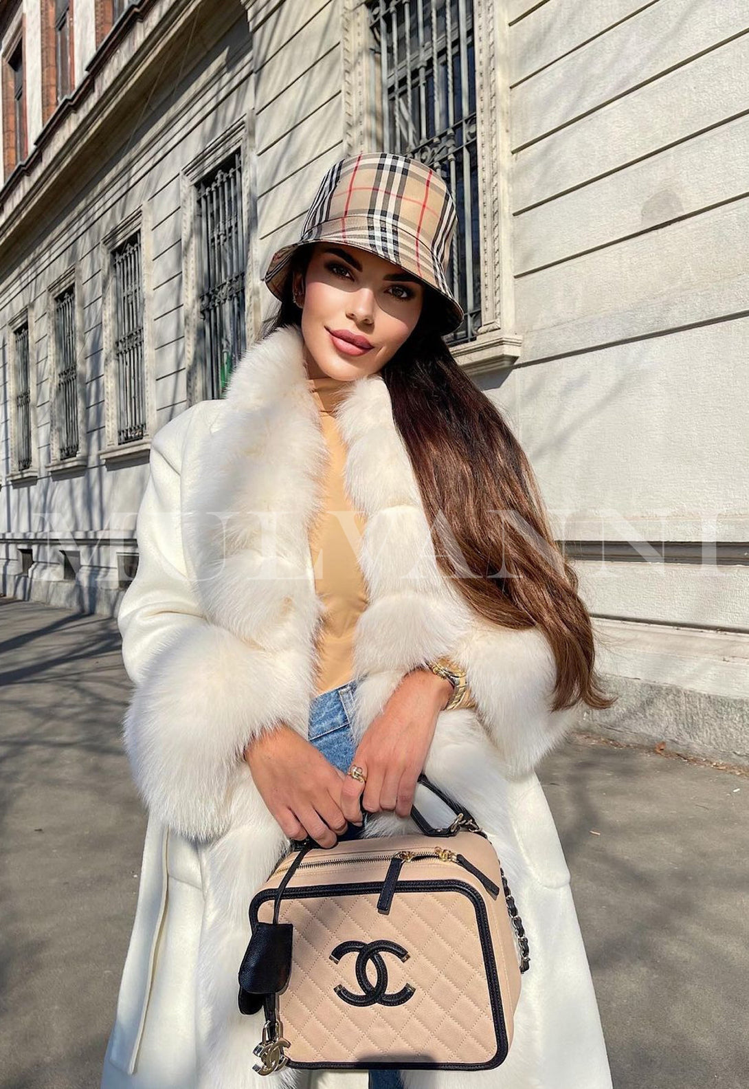 Woman wearing ALIZE white cashmere coat with fox fur trim, stylish winter outfit holding designer bag, standing on city sidewalk.