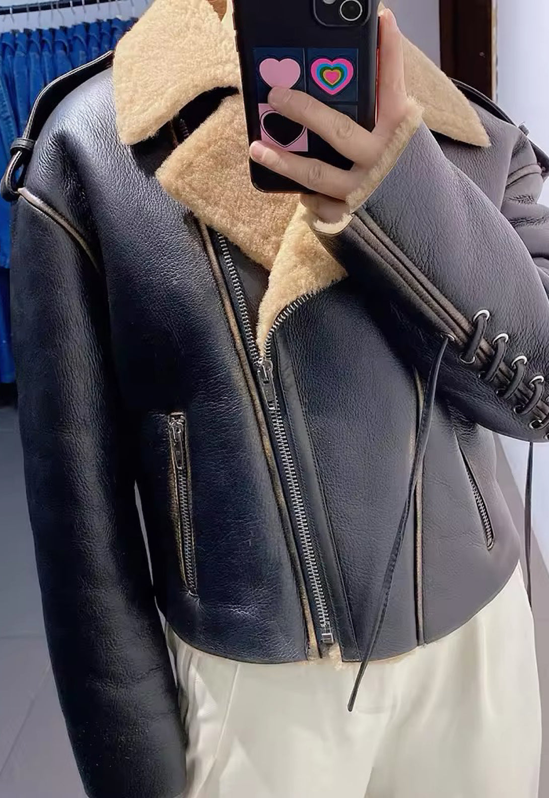 A woman wearing a black shearling jacket with a brown interior, crafted from high-quality leather.