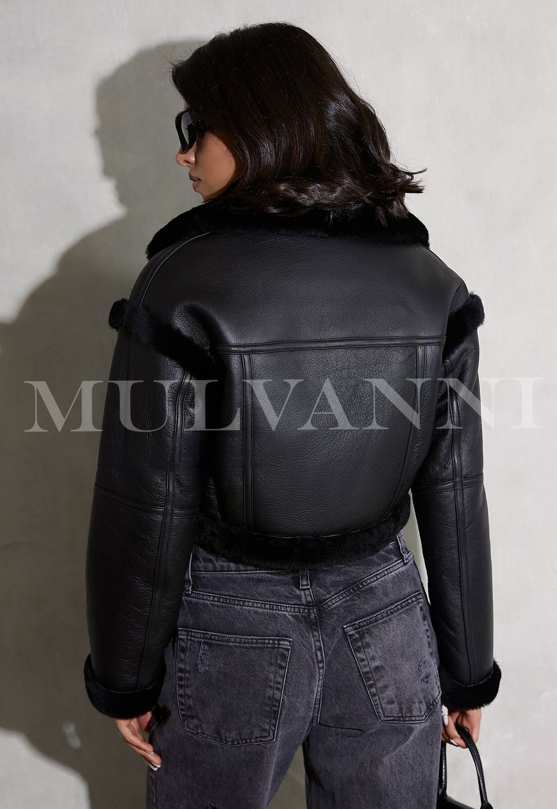 A woman wearing a cropped black shearling leather jacket, showcasing a sleek and edgy look for cooler days.