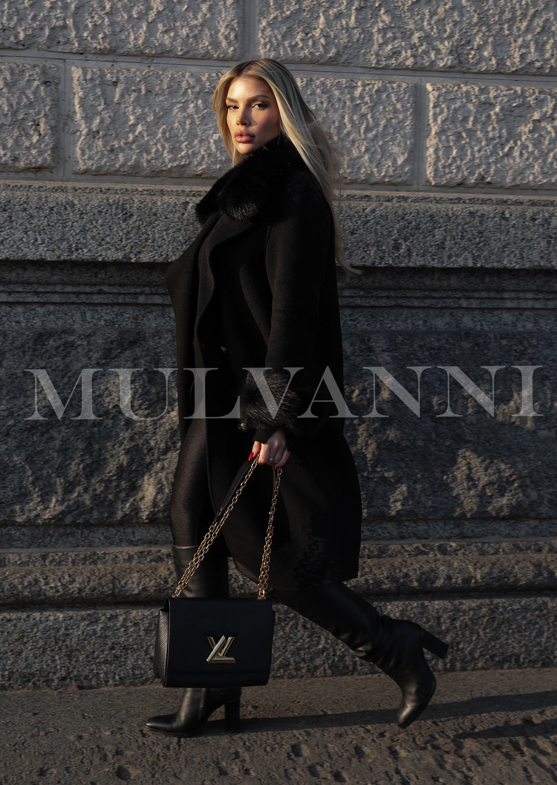 A stylish woman in a black cashmere coat featuring opulent fox fur accents, showcasing a perfect blend of comfort and high fashion. The coat enhances her winter ensemble with elegance.