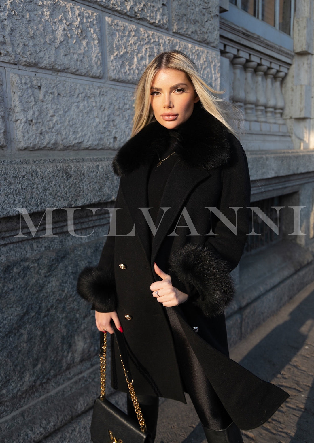 A woman wearing a luxurious black cashmere coat embellished with plush fox fur details. The coat’s elegant silhouette and rich texture provide a sophisticated look for winter outings.