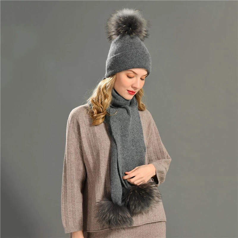 A woman wearing a grey cashmere scarf and pom pom fur hat designed by MVFURS